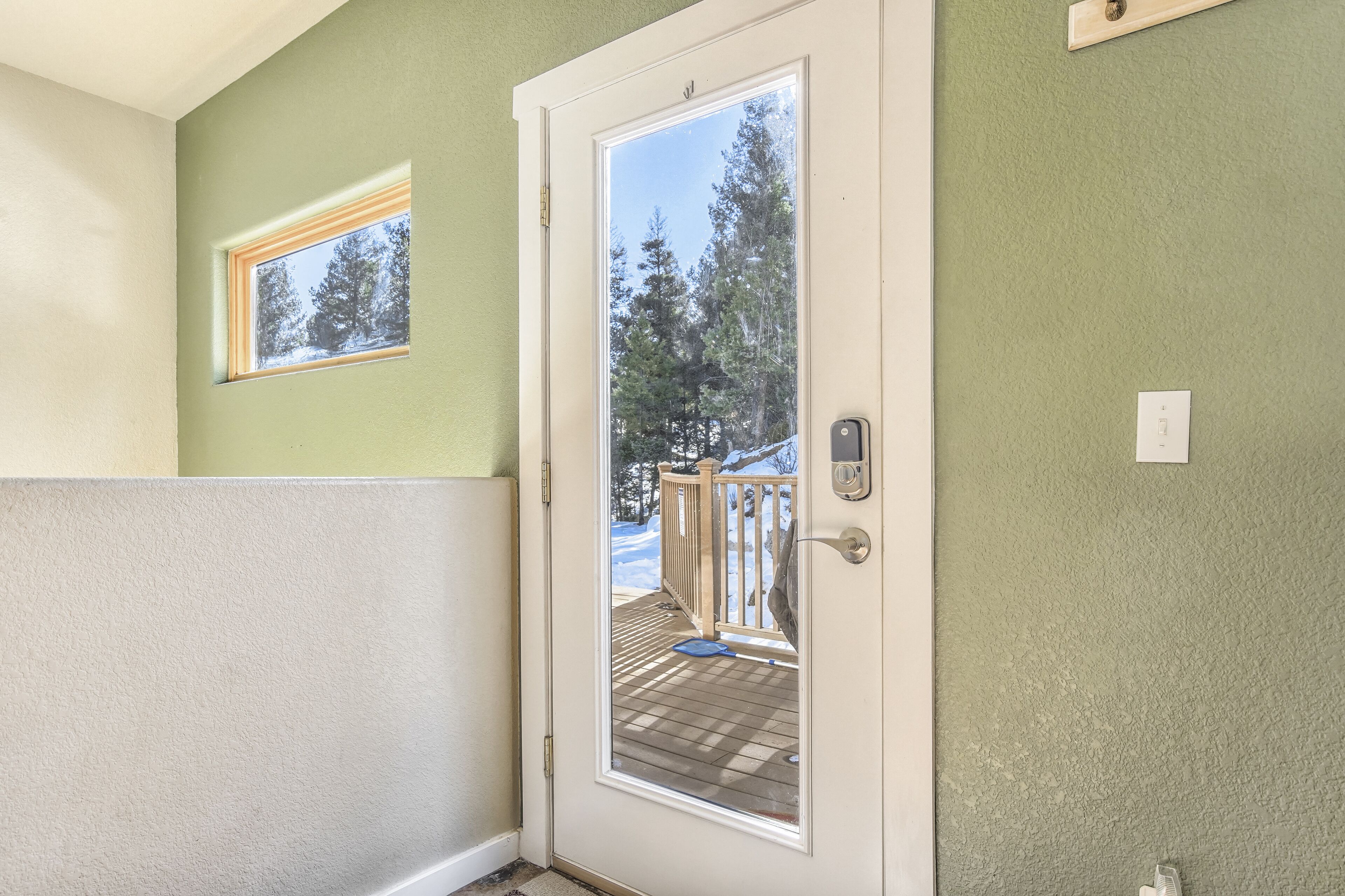 Une porte avec un panneau de verre, une petite fenêtre au-dessus, et une vue sur une terrasse dotée d’une balustrade.
