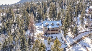A modern house with a large deck, surrounded by a dense forest and snow-covered ground. - Peekaboo Mountain (Cascade)