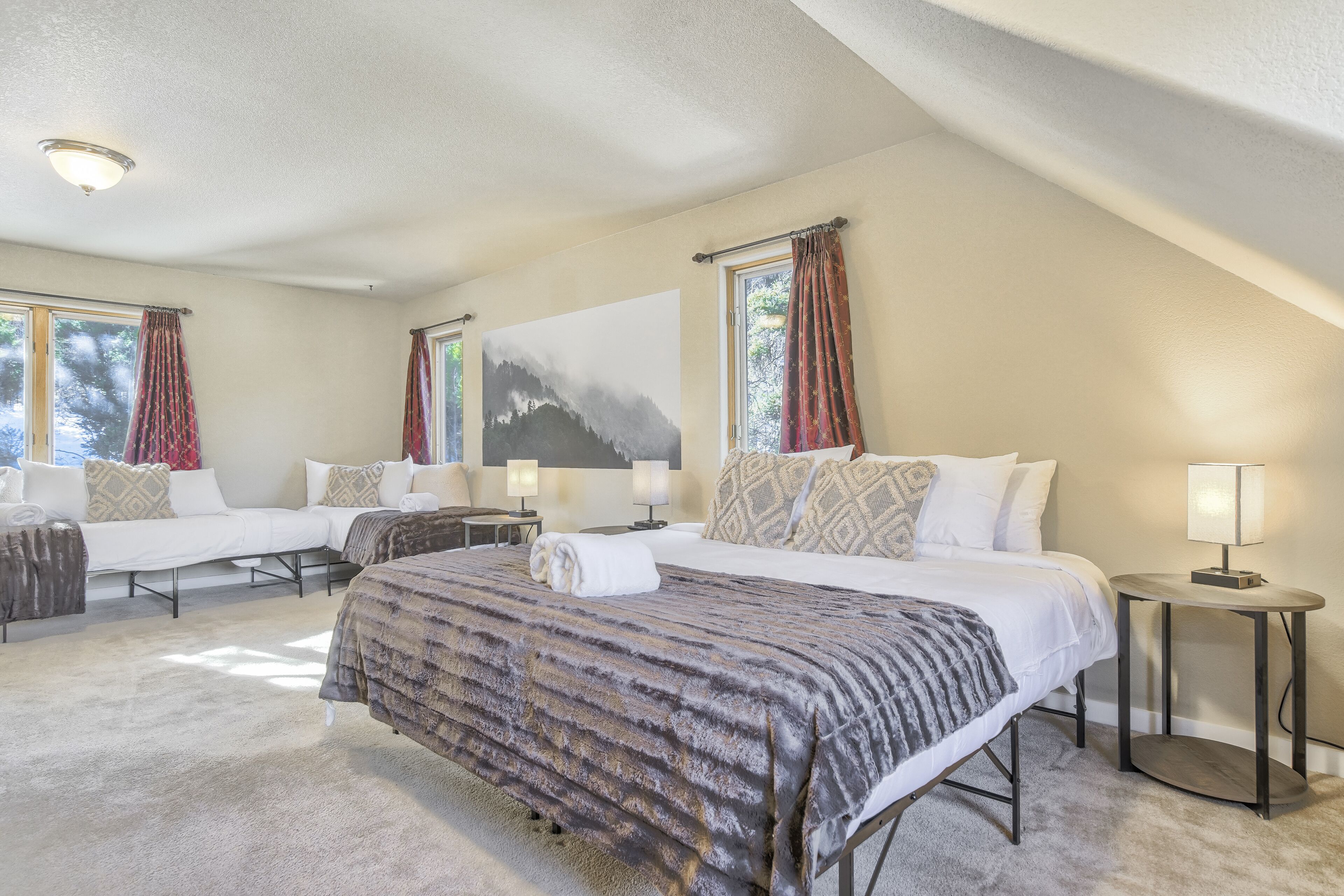 A hotel room with two beds, a large window, a painting, and a lamp.