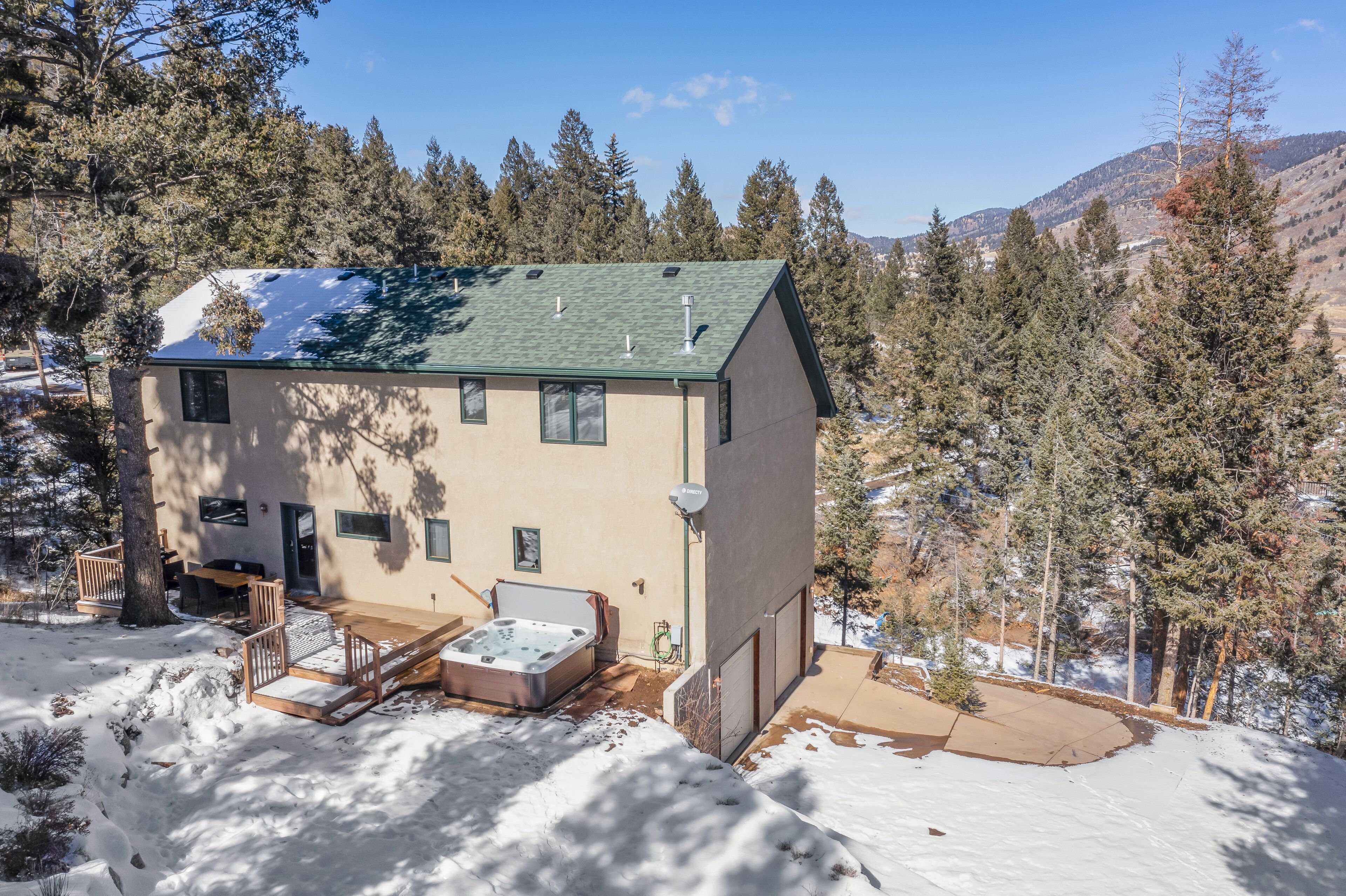 A two-story house with a green roof, a hot tub, and a deck.