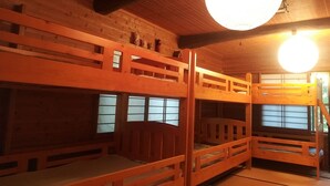 A wooden cabin with bunk beds, a large round light fixture, and a window with a view.