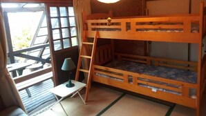 A bunk bed room with a ladder, a small table with a lamp, and a view of the outside through a window.
