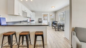 A modern kitchen with white cabinets, a granite countertop, and three wooden stools. - Sun-Soaked Okeechobee Retreat w/ Canal Views! (Okeechobee)