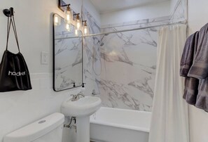 Un baño con pared de mármol, un lavamanos blanco, inodoro, bañera y toalla colgada.