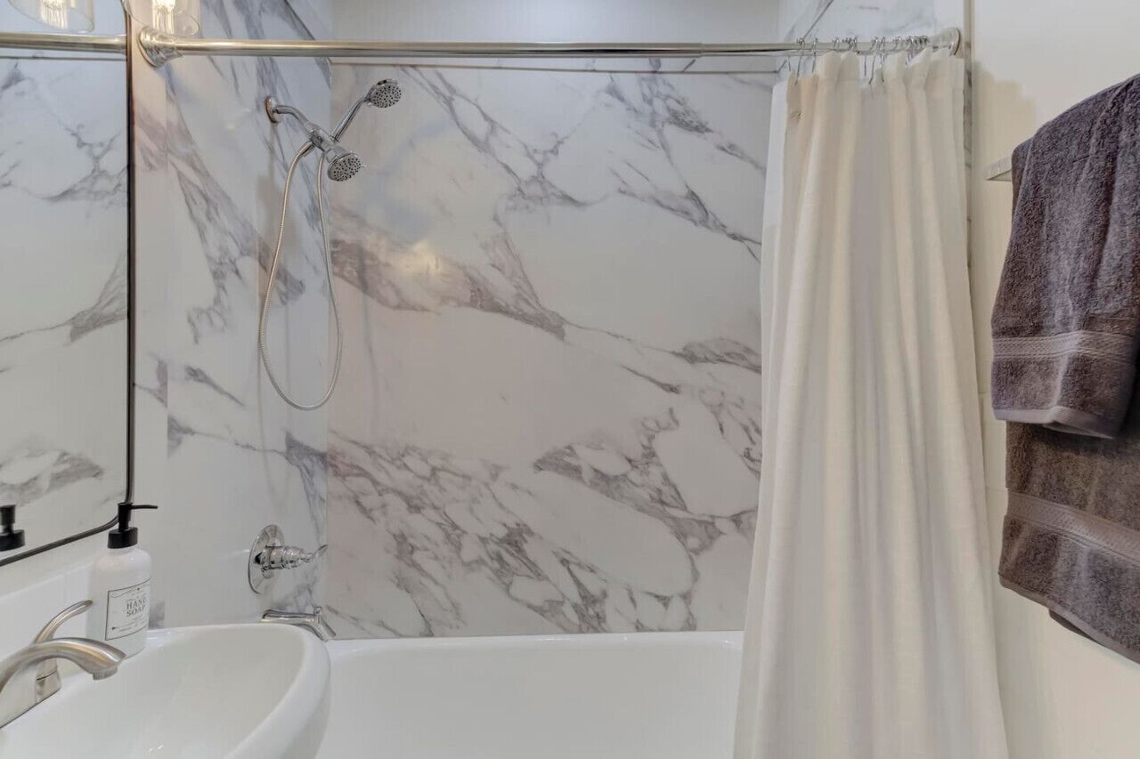 A bathroom with a marble shower wall, a bathtub, and a white sink.