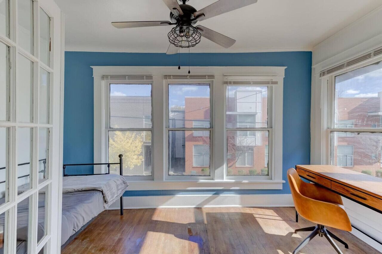 A room with a bed, a desk, and a ceiling fan.