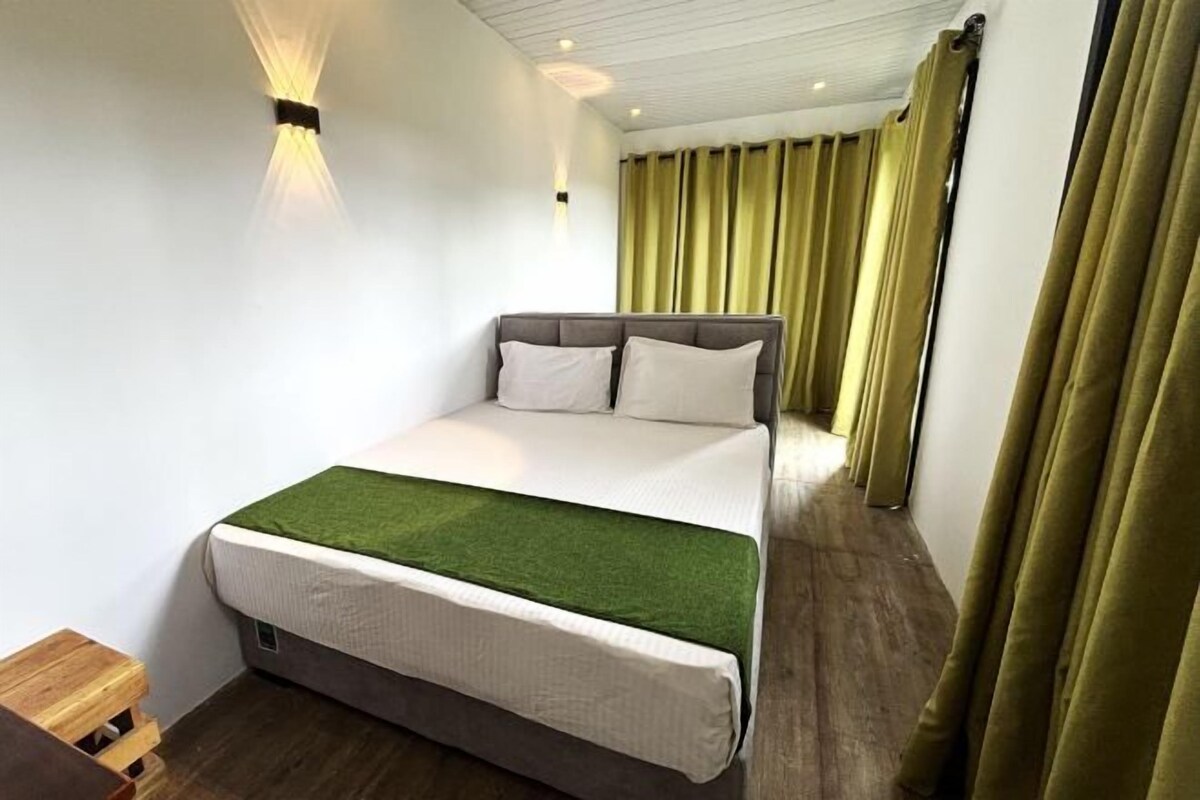 A neatly arranged hotel room with a bed, a small wooden stool, and a green throw blanket.