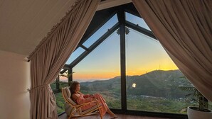 A room with a large window offering a view of a hilly landscape during sunset. - The Blackberry Cottage (Nuwara Eliya)