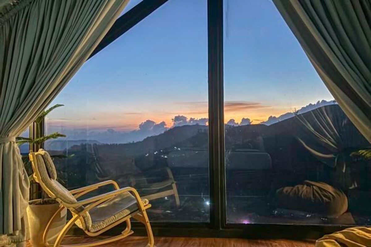 Une pièce dotée d’une grande fenêtre donnant sur un paysage montagneux au coucher du soleil.