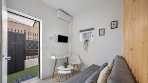 Ein modernes Wohnzimmer mit einer grauen Couch, einem kleinen weißen Tisch, einem Fernseher und einer Holztür.