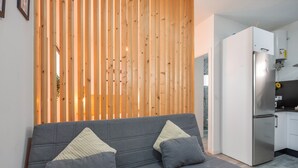 Ein modernes Wohnzimmer mit grauem Sofa, Holzlatten, einem weißen Kühlschrank und einer Küchenzeile.