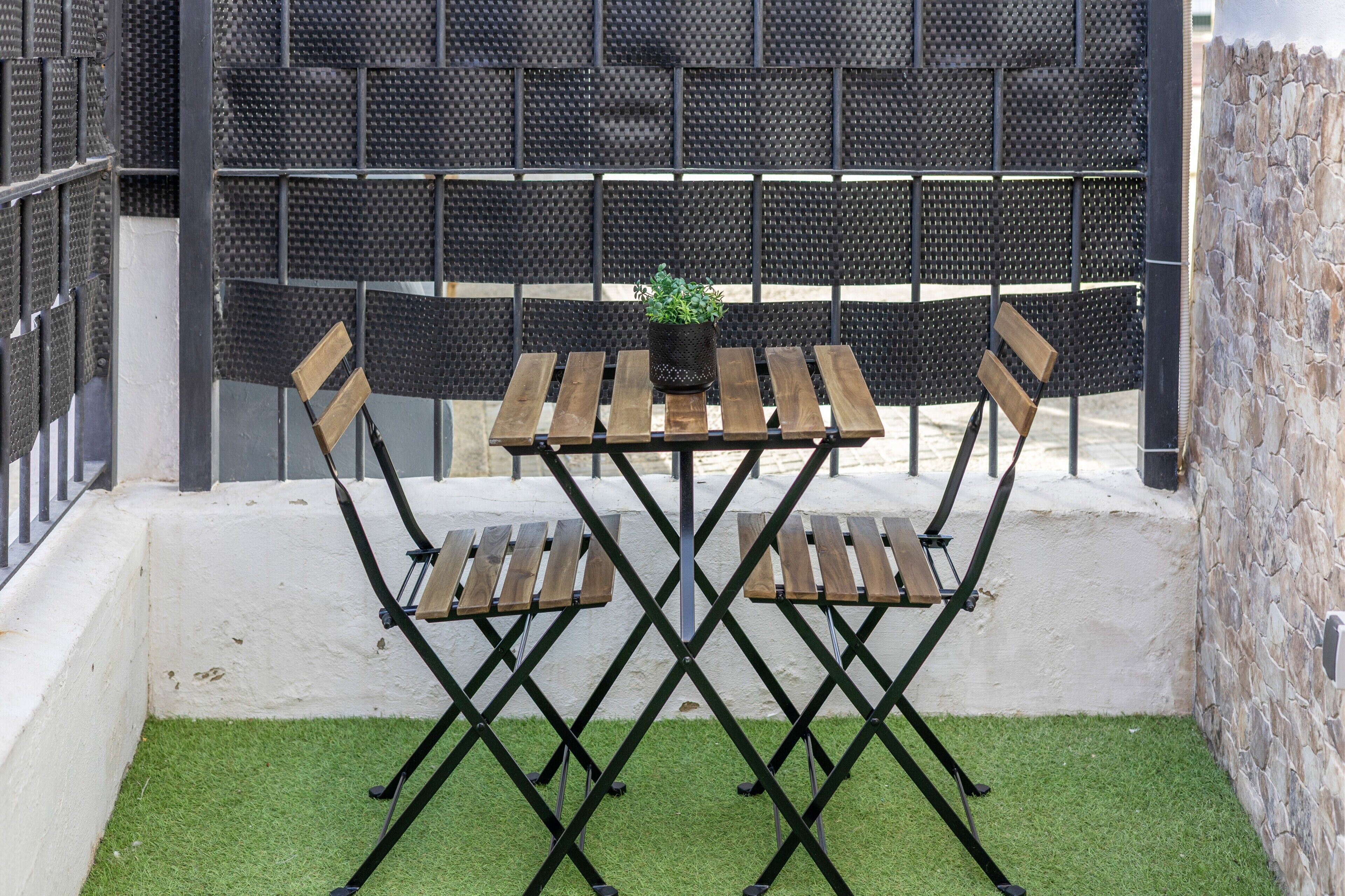 Une terrasse avec une table et des chaises, une plante en pot et un mur à motifs en arrière-plan.
