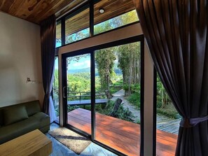 Una habitación con un amplio ventanal corredera que da a una terraza exterior con un sendero de madera y vegetación.