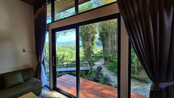 A room with a large sliding glass door leading to an outdoor deck with a wooden pathway and greenery.