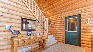A wooden interior with a staircase, a wooden console table with drawers, a framed picture, and a green door. - Hill Road Chalet on Benoit Lake in Spooner WI (Spooner)