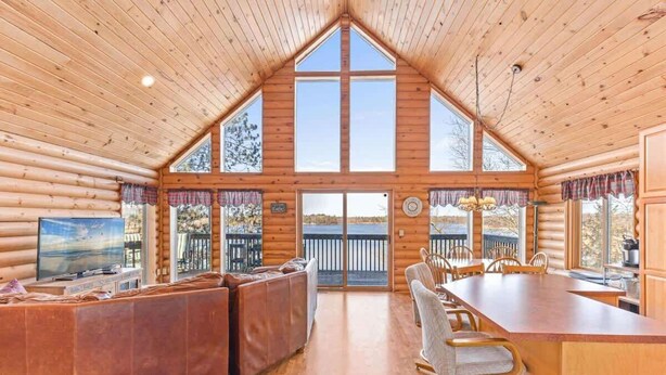 A log cabin interior with a large dining area, a sofa, and a TV. - Hill Road Chalet on Benoit Lake in Spooner WI (Spooner)