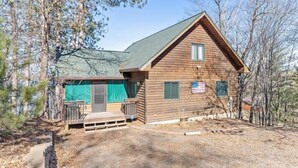 A wooden cabin with a green roof, a front porch, and an American flag. - Hill Road Chalet on Benoit Lake in Spooner WI (Spooner)