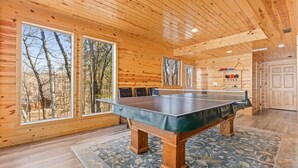 A wooden interior with a ping pong table, large windows, and a view of trees. - Hill Road Chalet on Benoit Lake in Spooner WI (Spooner)