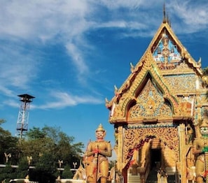 A temple with intricate architecture and a tall structure in the background. - My Room Nakhonpathom (Nakhon Pathom)
