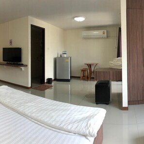 A hotel room with a bed, a television, a refrigerator, a small table, and a chair.
