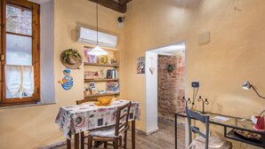 A dining area with a table set for two, a hanging light fixture, a brick wall, and a wooden ceiling. - Holiday Home 'La Casa Gialla Di Buonconvento' with Wi-Fi and Air Conditioning (Buonconvento)