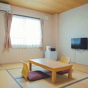Una habitación con suelo de tatami, una mesa de madera, dos sillas, un televisor y un pequeño electrodoméstico blanco.