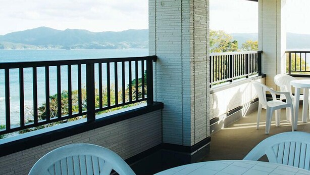 Een balkon met witte stoelen en een tafel, met uitzicht op een wateroppervlak en heuvels in de verte.
