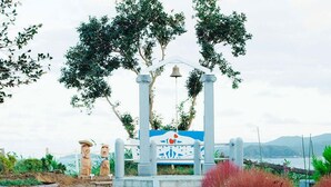 Een tuinpad leidt naar een prieel met een klok, omringd door potplanten en uitzicht op de zee.