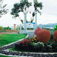 Un sendero en un jardín conduce a un pabellón con una campana, rodeado de plantas en macetas y vistas al mar.