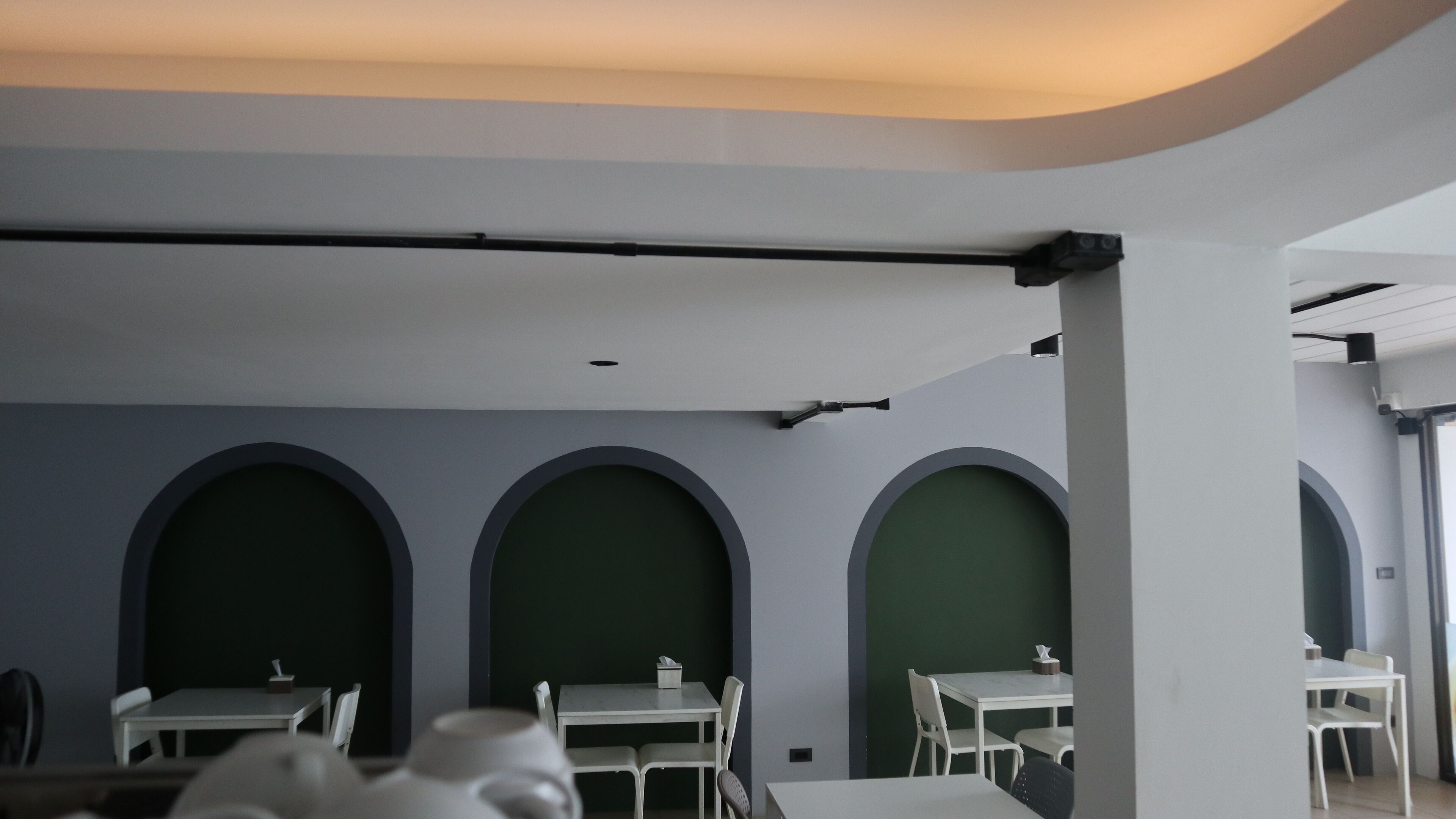 A modern interior with white tables and chairs, green accent walls, and a curved ceiling.