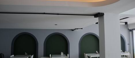 A modern interior with white tables and chairs, green accent walls, and a curved ceiling.
