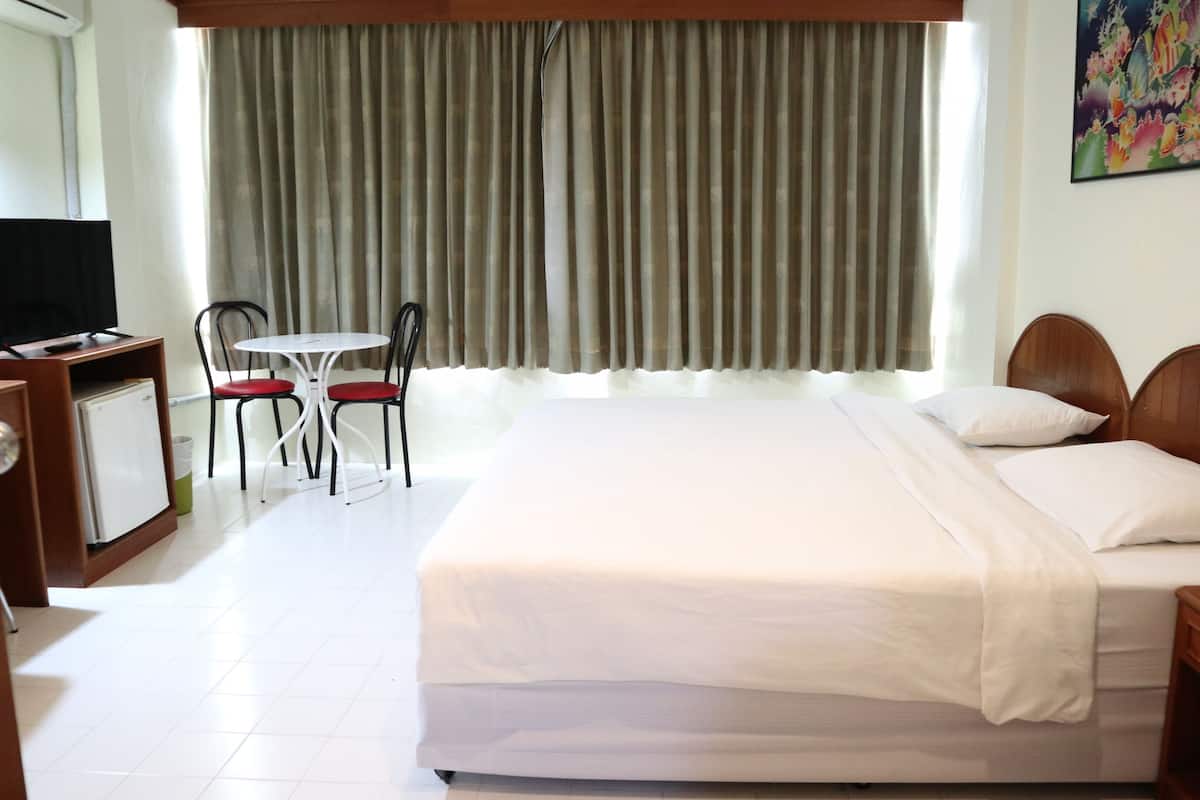 Une chambre d’hôtel avec un lit, un bureau avec une télévision, une chaise et une fenêtre avec des rideaux.
