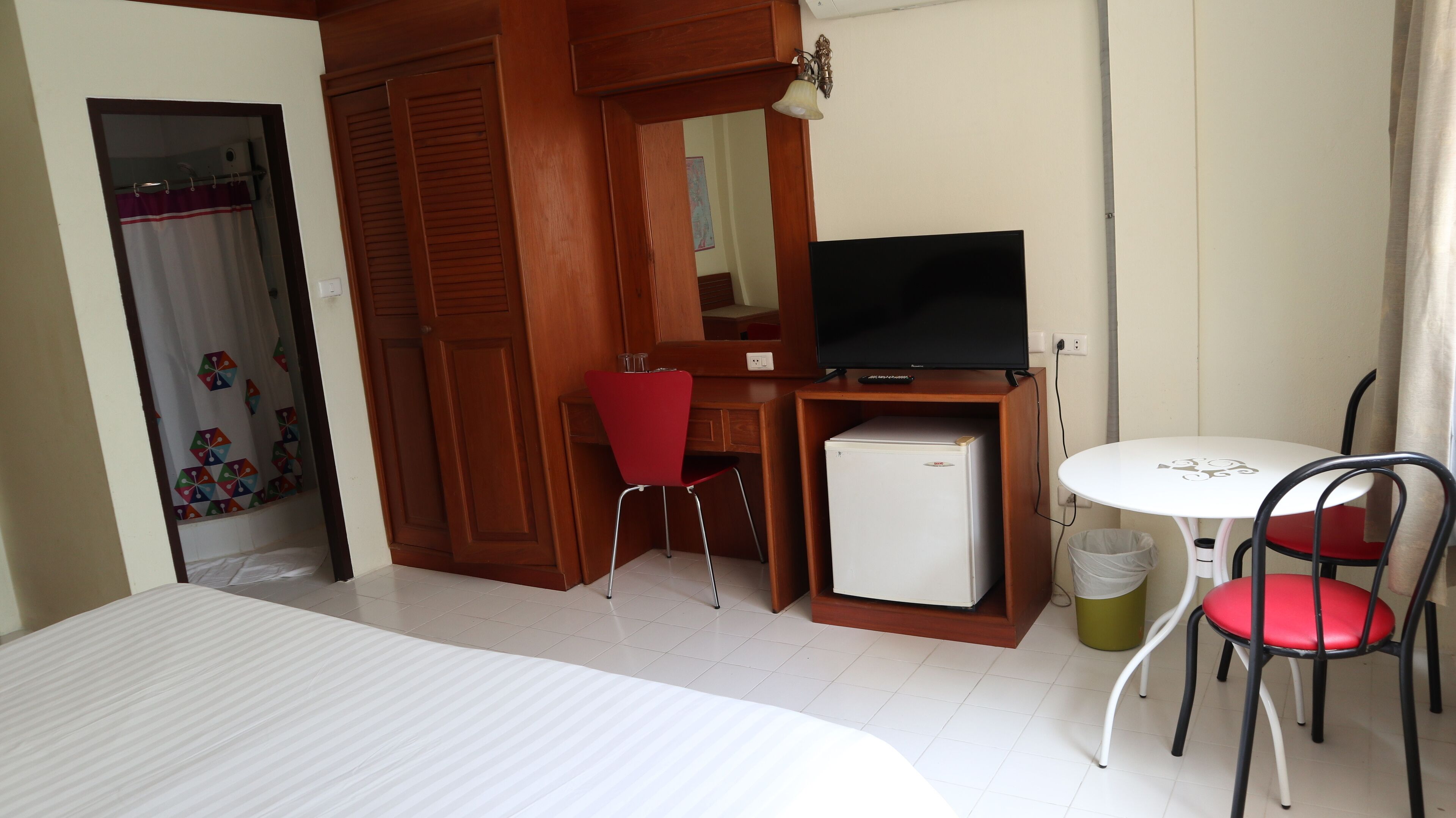 A hotel room with a bed, a desk with a television, a small refrigerator, and two chairs.
