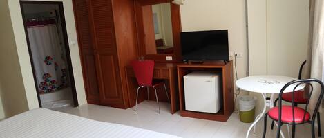 A hotel room with a bed, a desk with a television, a small refrigerator, and two chairs.