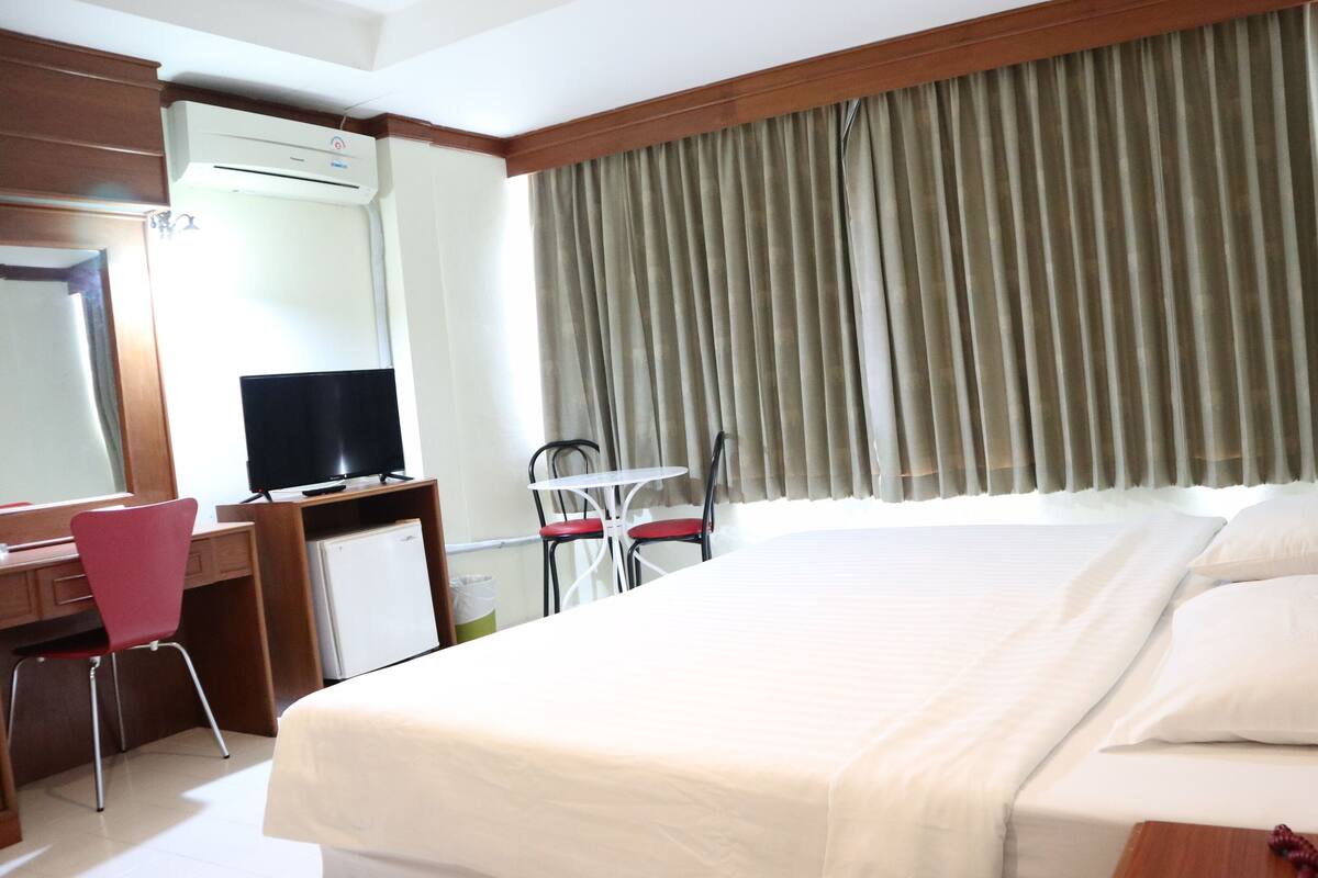 Une chambre d’hôtel équipée d’un lit, d’un bureau, d’une chaise, d’une télévision et d’une fenêtre avec des rideaux.