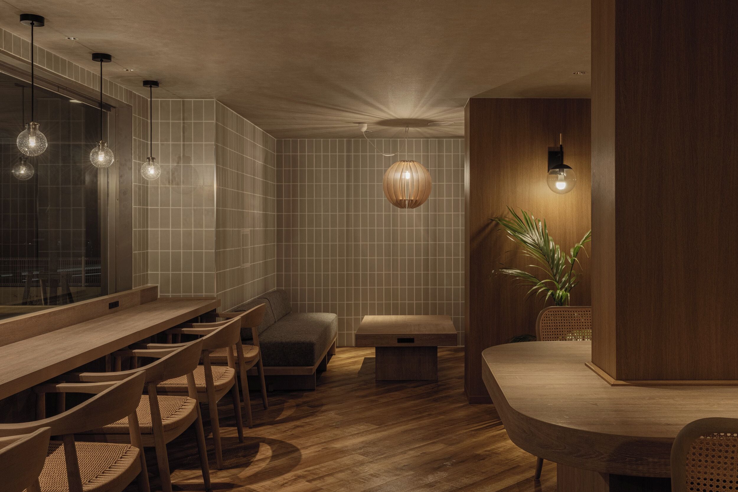 A modern interior with a long wooden table and chairs, a bench, and a hanging light fixture.
