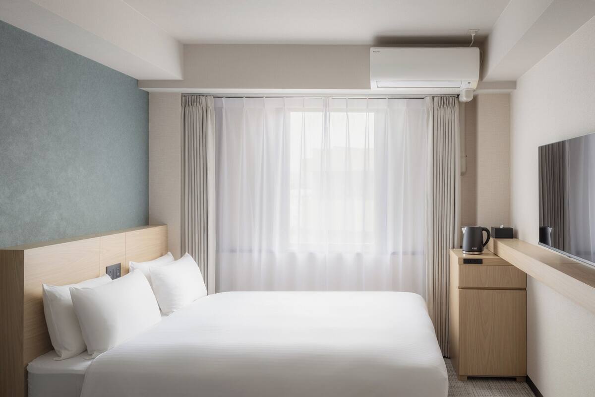 Ein Hotelzimmer mit Bett, kleinem Schreibtisch, Fernseher und einem Fenster mit Vorhängen.