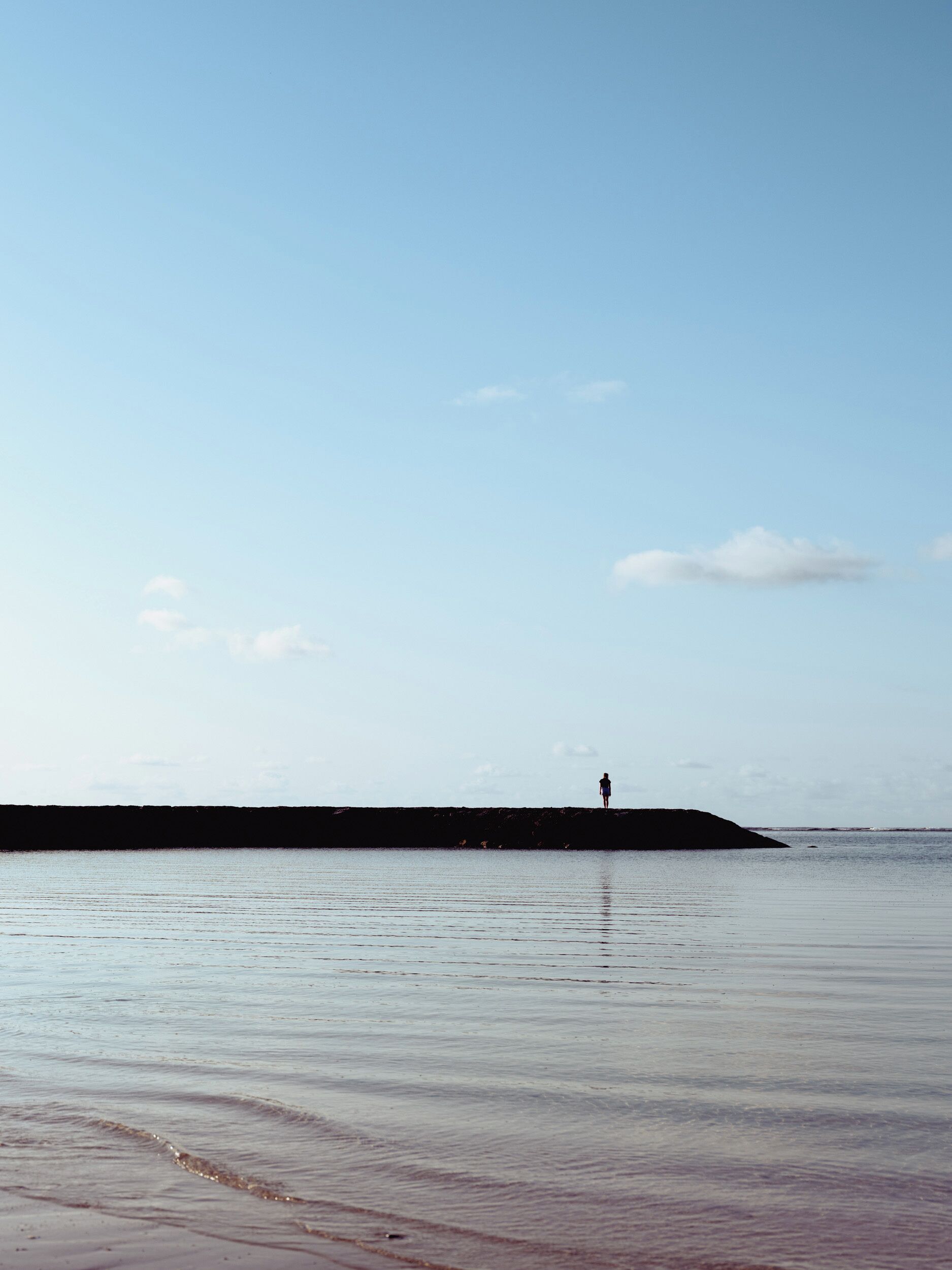 A person standing on a pier extending into calm water.