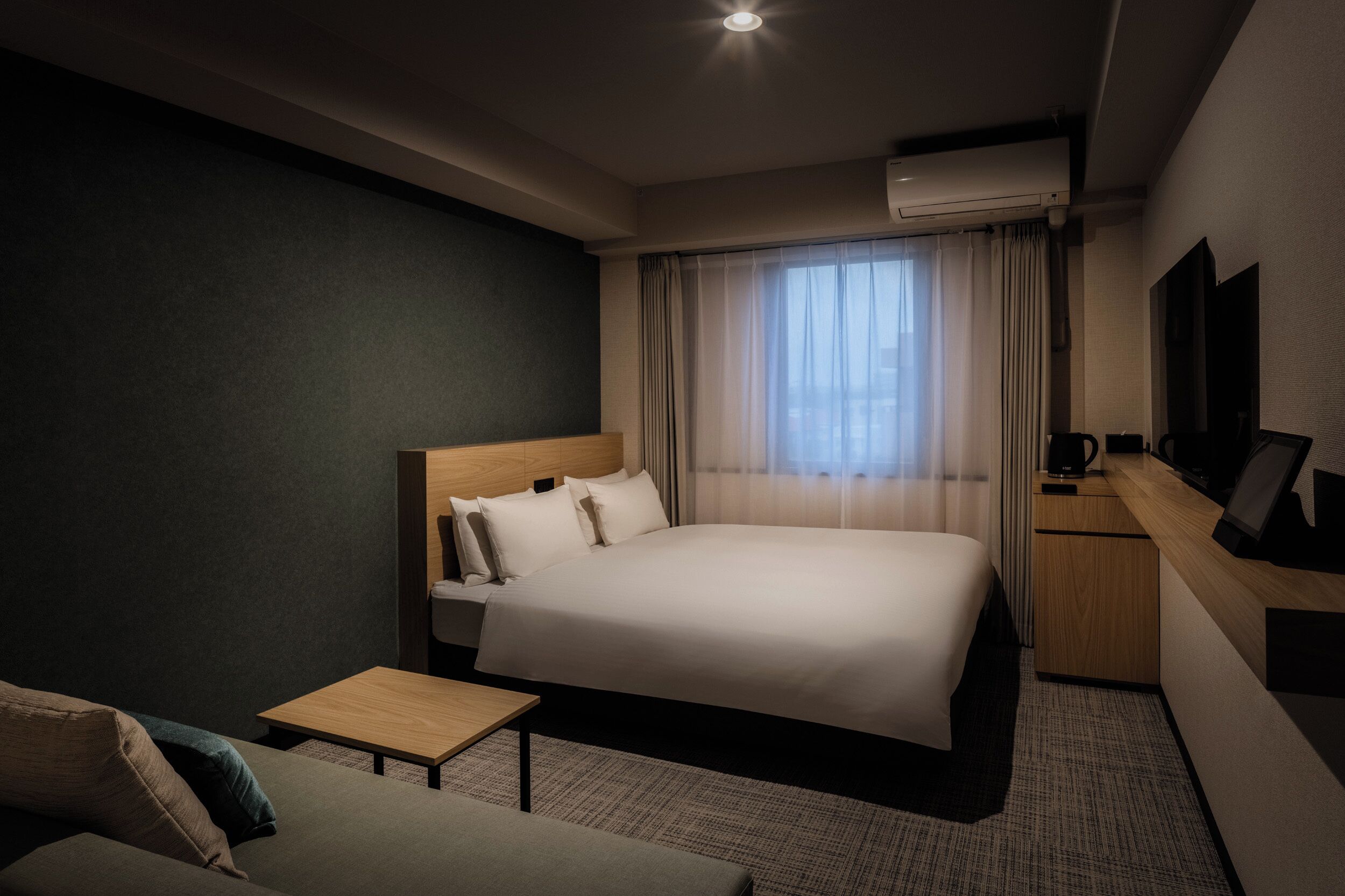 A hotel room with a bed, a small table, a sofa, a desk, and a TV.