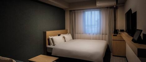 A hotel room with a bed, a small table, a sofa, a desk, and a TV.