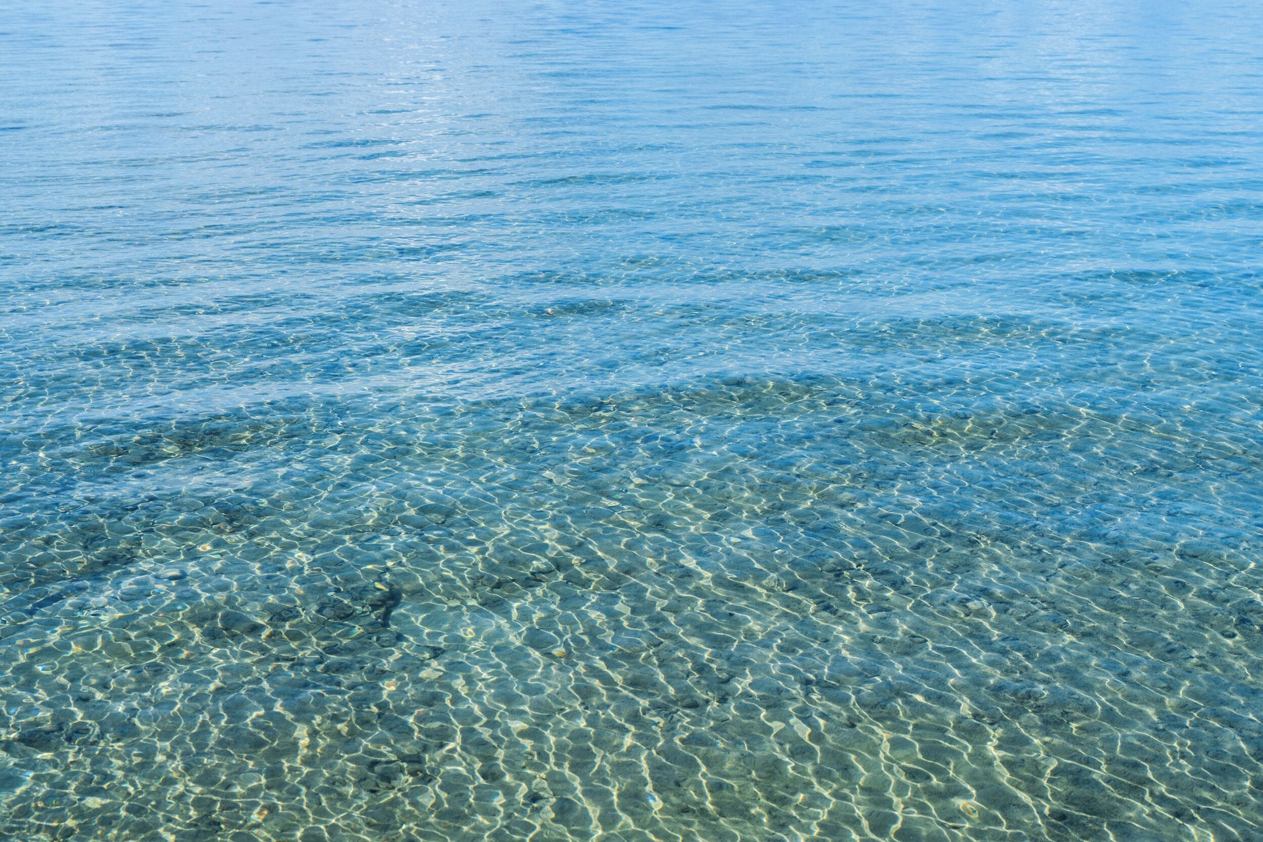 A clear view of a calm body of water with visible ripples and a sandy bottom.