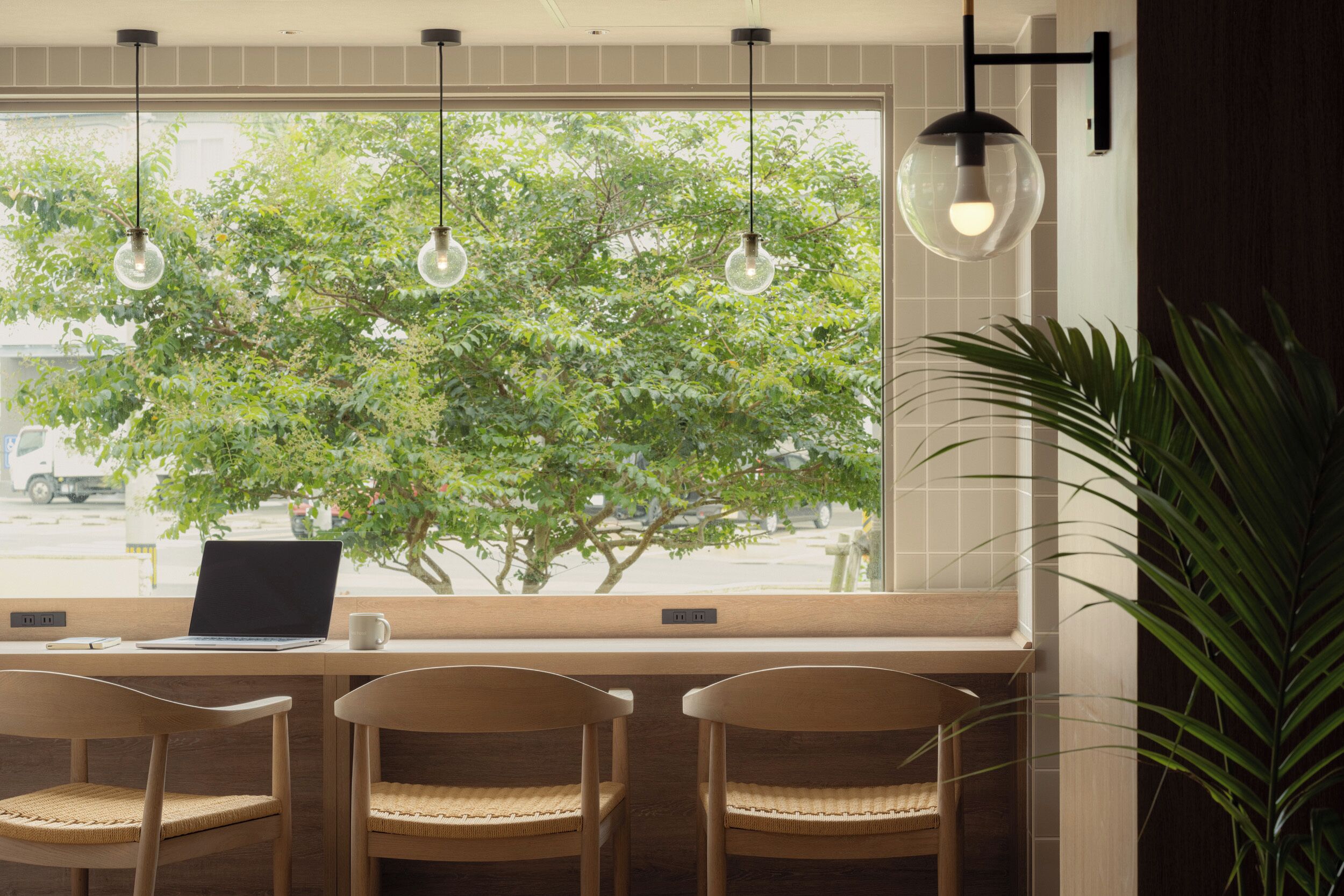 A workspace with a laptop, two chairs, and a large window with a view of a tree and parked cars.