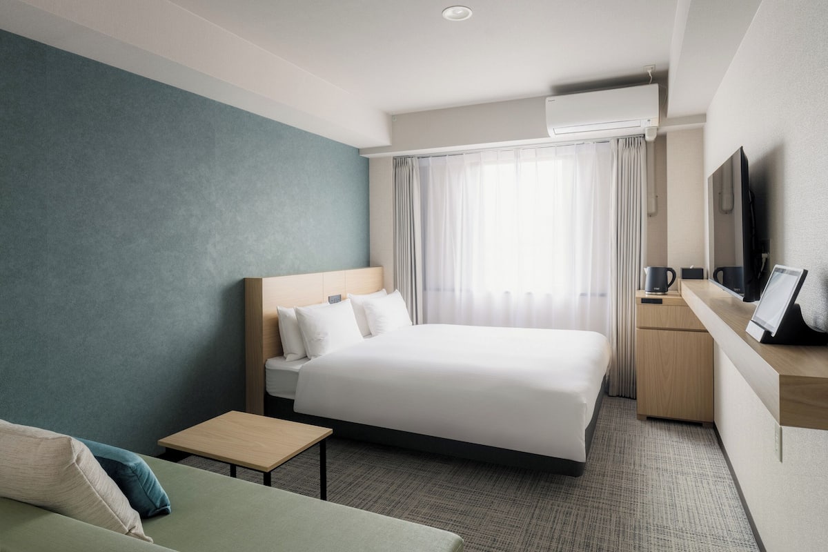 Ein Hotelzimmer mit Bett, einem kleinen Tisch, einem Fernseher und einem Schreibtisch mit Stuhl.