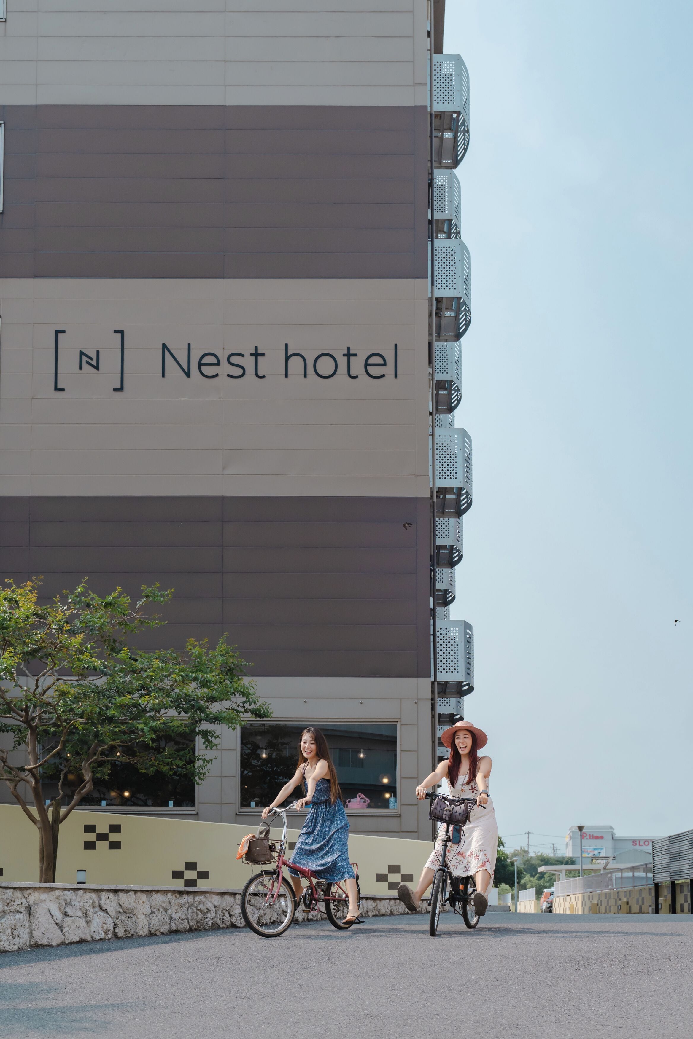 A building with a sign reading 'Nest hotel' and a tree in the foreground.