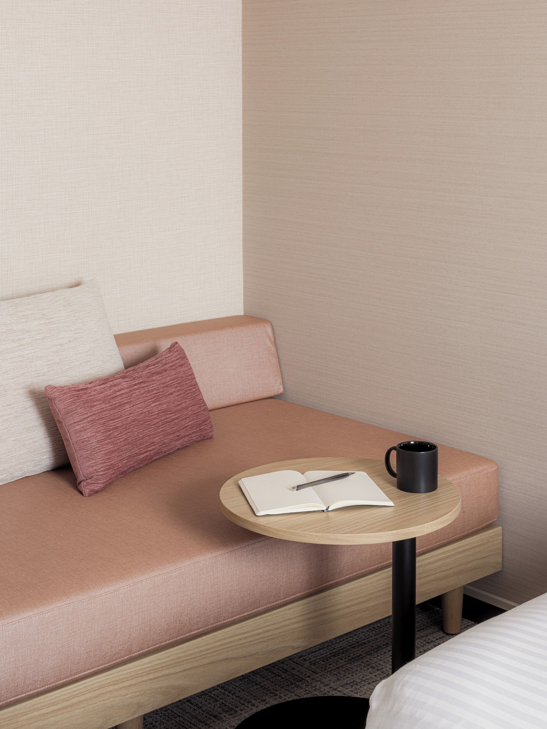 Habitación de hotel con un sofá, una pequeña mesa redonda, una taza negra y un cuaderno.