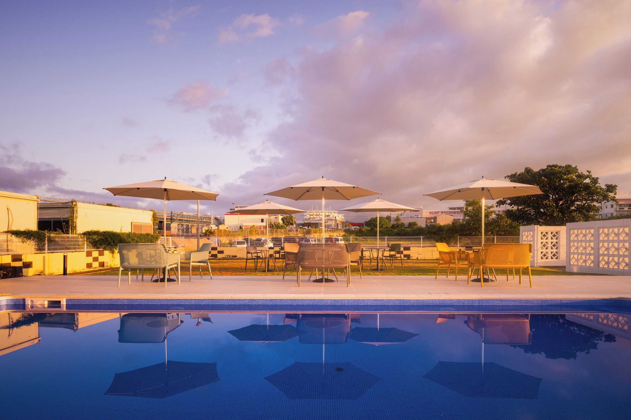 Une piscine entourée de bâtiments, avec des chaises longues et des parasols.