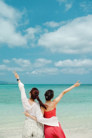 Two people standing at a beach with a clear sky and ocean in the background. - Nest Hotel Ishigaki Maesato Beach (Ishigaki)