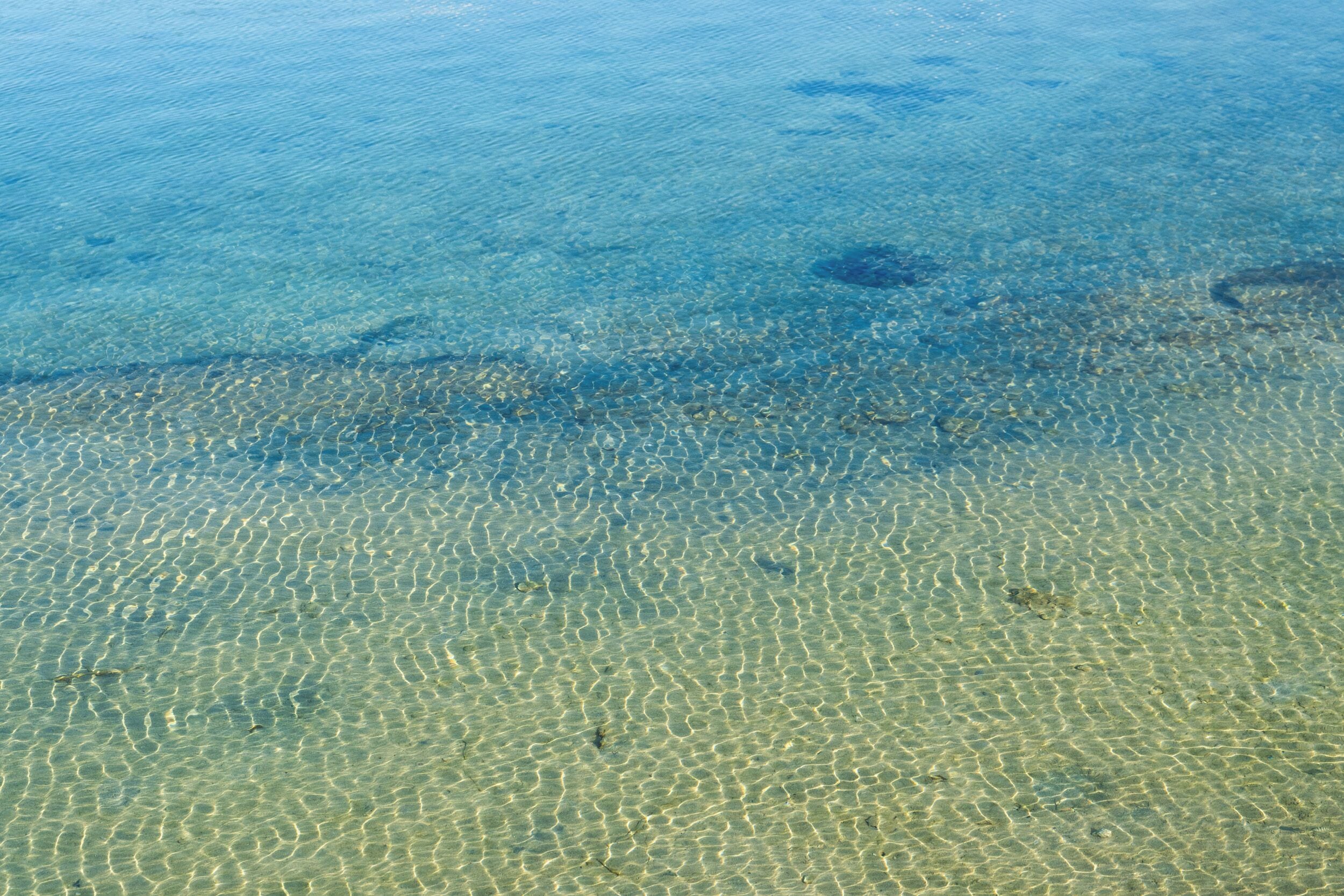 Vista despejada de una playa con aguas poco profundas y dibujos de arena visibles.