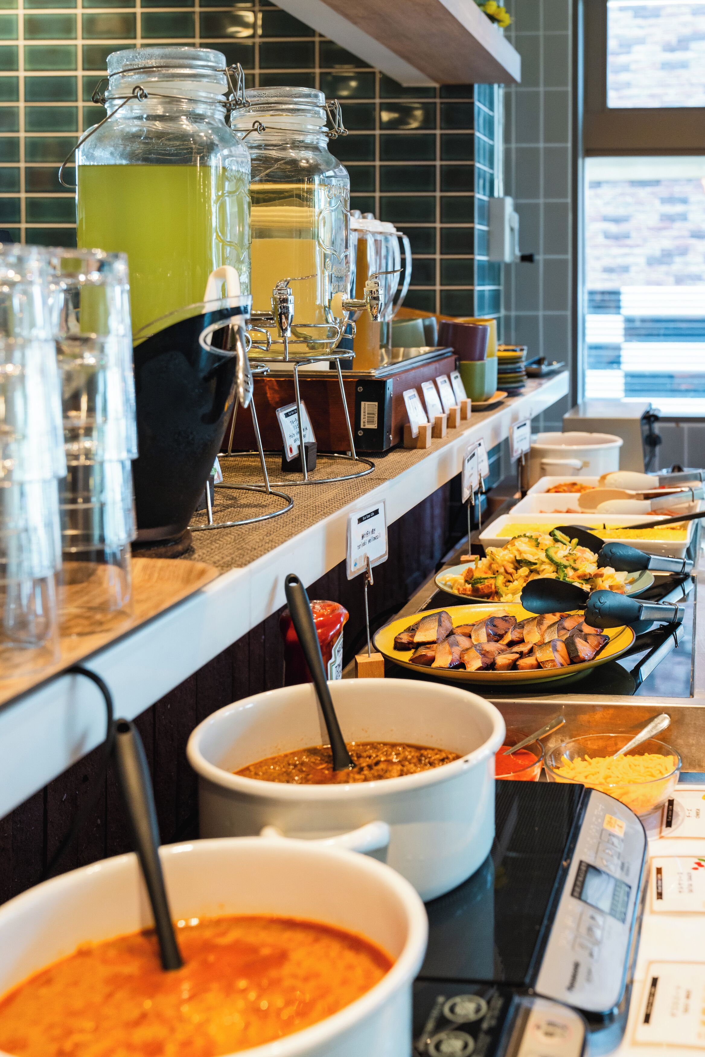 A buffet with various food items and beverages, including a large pot of soup, a bowl of chili, and several containers of salad.