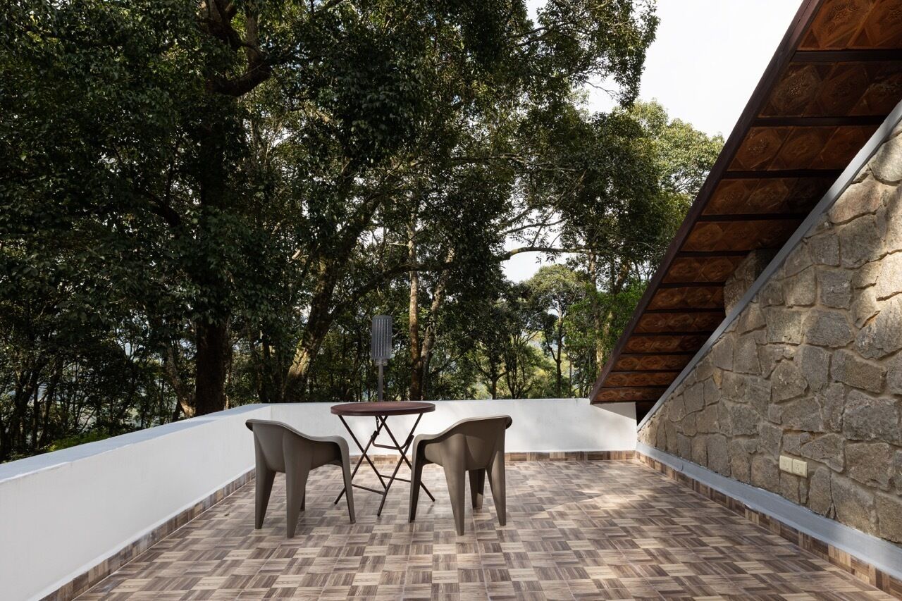A patio with a table and chairs, surrounded by trees and a stone wall.